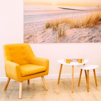 Gemütliches Regiezimmer mit gelbem Sessel, weißen Tischen und Strandbild.