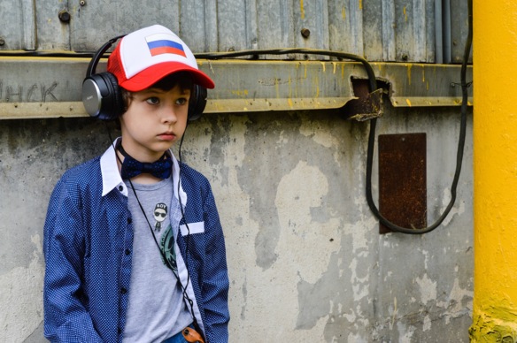 Gebannt schauender Junge mit aufgesetzten Kopfhörern, an eine Wand gelehnt