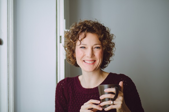 Foto von Ann, mit Teebecher in der Hand in die Kamera lächelnd