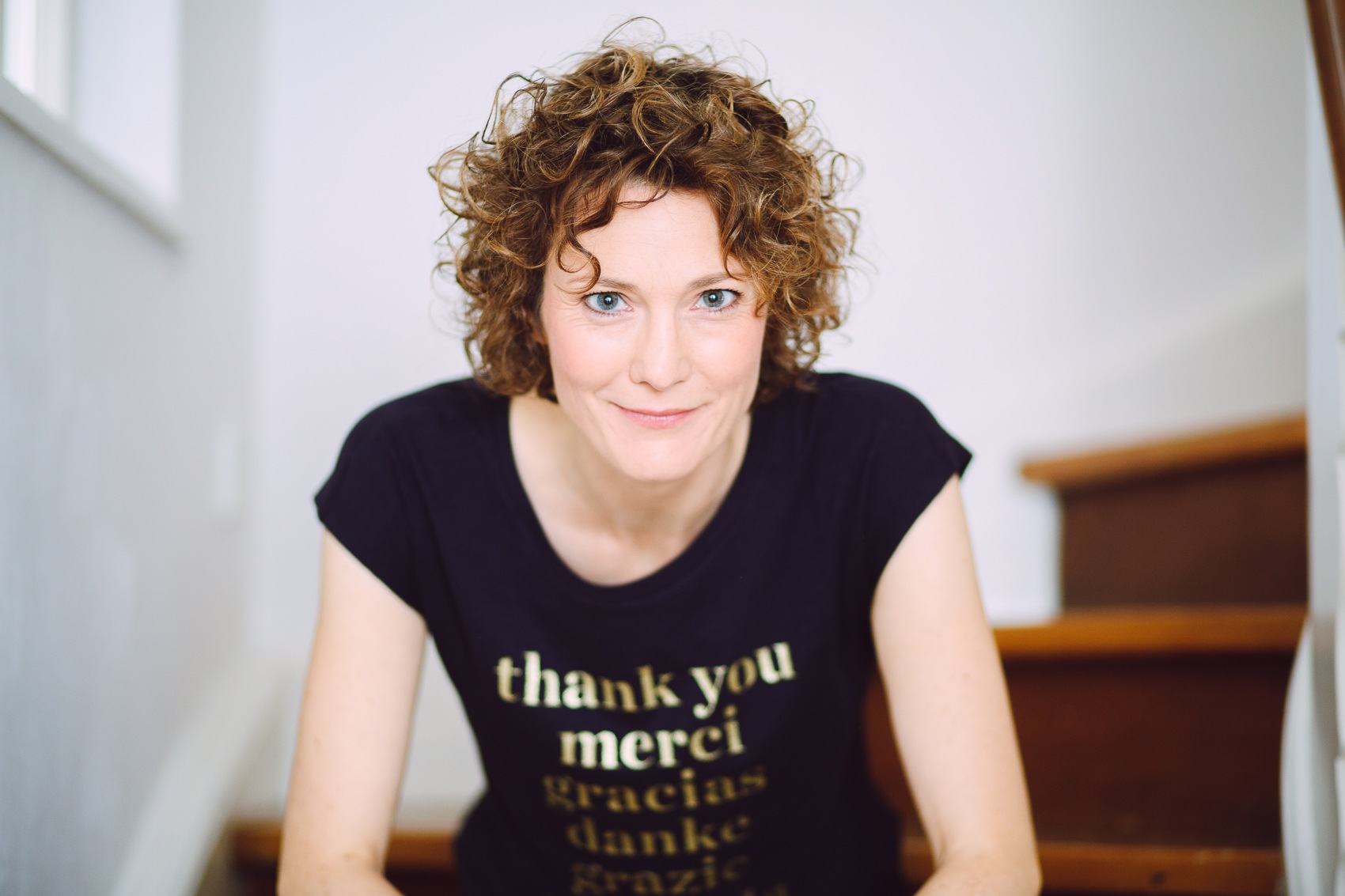 Porträt von Ann Vielhaben, wie sie auf einer Treppe sitzt und neugierig direkt in die Kamera schaut.