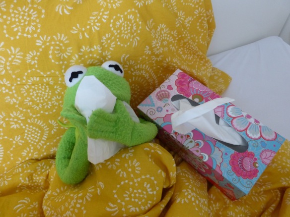Kermit der Frosch liegt mit Taschentuch krank unter Bettdecke