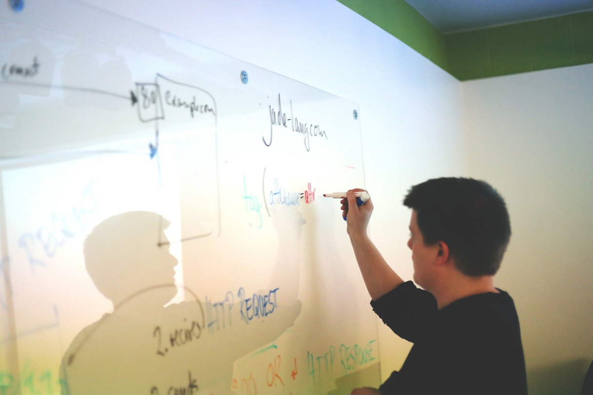 A young man writes formulas on a white board
