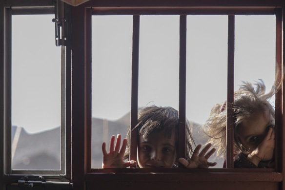 Two curious little children look through a window with bars