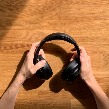 Nahaufnahme meiner Hände, die hochwertige Austrian Audio Hi-X55 Kopfhörer auf einem Holztisch halten.