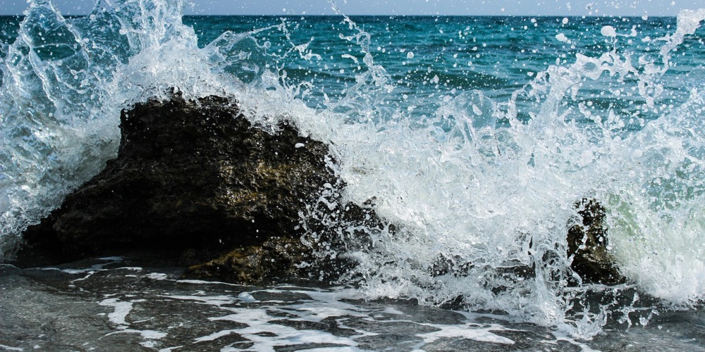 An ocean wave breaks on a small rock near the shore