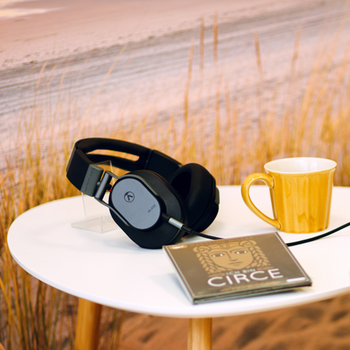 Headphones, CD case, and mug on a small side table with a beach photograph in the background.