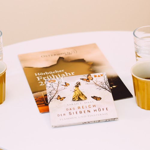 Hörbuch-CD "Das Reich der sieben Höfe" gesprochen von Ann Vielhaben, liegend auf einem Tisch neben Kaffeetassen.