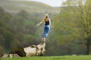 Young woman in back view, practically throwing herself off a tree trunk into the grass