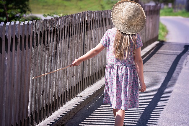 Girl from behind riding along a fence with a stick in her hand